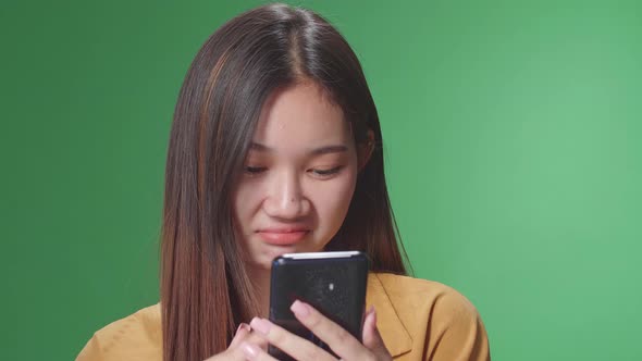 Asian Woman Emotionally Flipping Something On The Phone While Standing In The Green Screen Studio