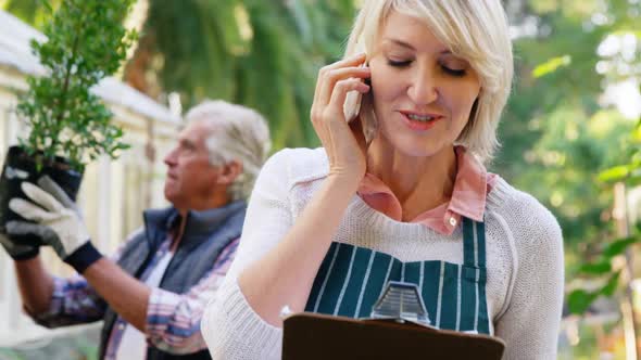 Mature woman talking on phone while man checking vegetables