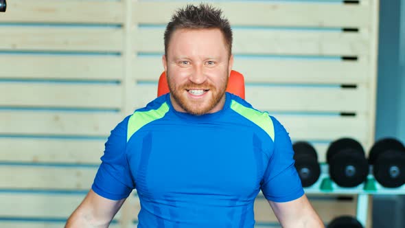 Muscular Man Doing Exercises with Dumbbells at Biceps in Gym