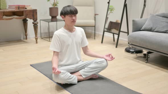 Young Asian Man Meditating on Yoga Mat at Home