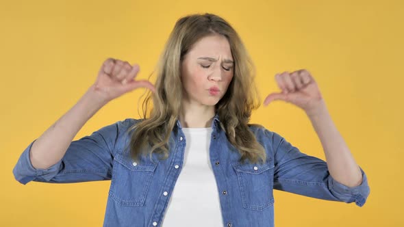 Portrait of Young Pretty Girl Gesturing Thumbs Down on Yellow Background