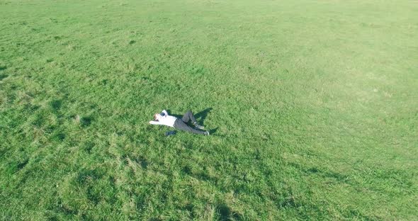 Low Orbital Flight Around Man on Green Grass with Notebook Pad at Yellow Rural Field