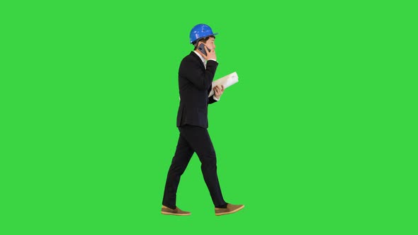 Middle Age Architect Man Talking on the Smartphone and Holding Blueprints While Walking on a Green