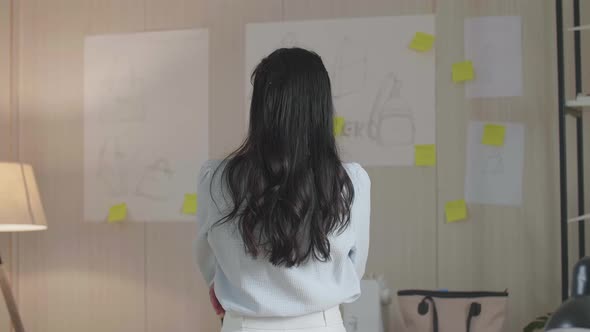 Asian Woman Designer Looking At The Design Sketch Paper On The Wall