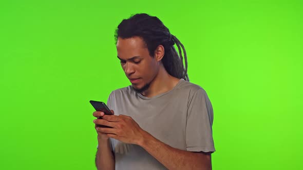 Young Excited African American Man Quickly Typing on Phone Stands on Studio