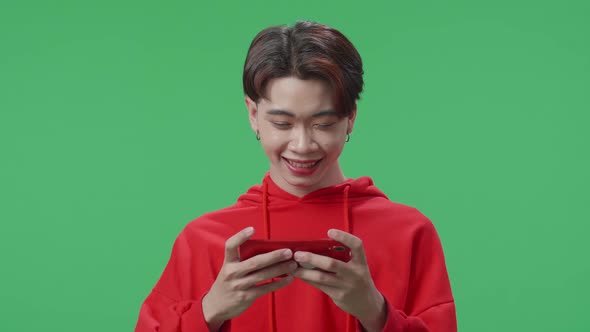 Smiling Asian Transgender Male Using Mobile Phone Playing Game While Standing In The Green Screen