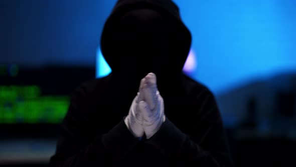 Silhouette of Unrecognizable Hacker in Black Hoodie Rubbing Hands in White Gloves