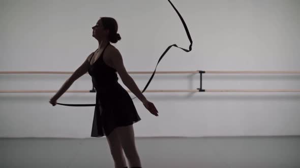 Silhouette of Girl in Black Dress and Pointe Shoes Perform Gymnastics Exercise with a Ribbon on a