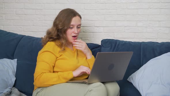 Woman is Sitting on the Sofa with Laptop and Typing Something