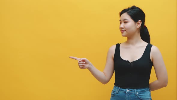 Young Excited Asian Woman Pointing Finger on an Empty Space, Yellow Background