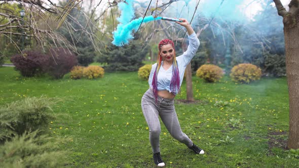 Beautiful Girl in with Multicolored African Braids Posing with Blue Smoke Against the Background of