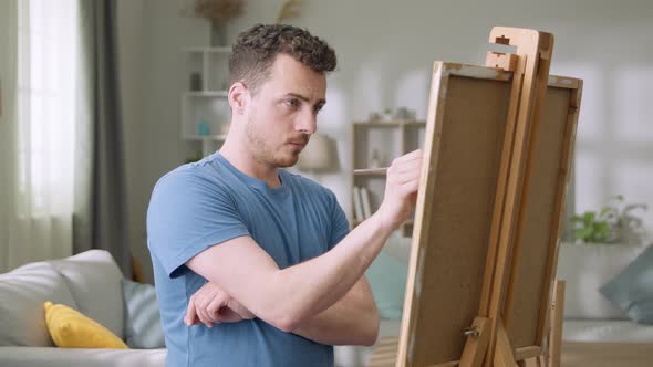 Young Man is Working in His Modern Home Studio in the Morning Drawing on Canvas Enjoying the Process