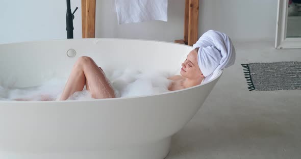 Attractive Delighted Woman Reclining in Bathtub Enjoying Day Off Taking a Bubble Bath at Home