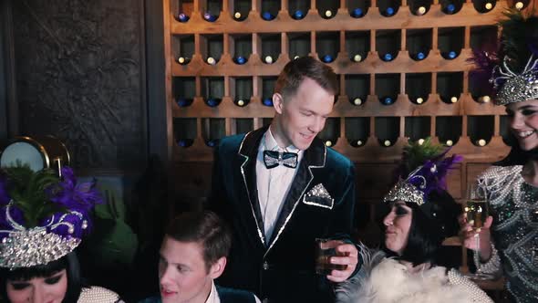 Theme Party - People in Glistening Clothes Sitting Behind the Table - A Man in the Centre Raises a