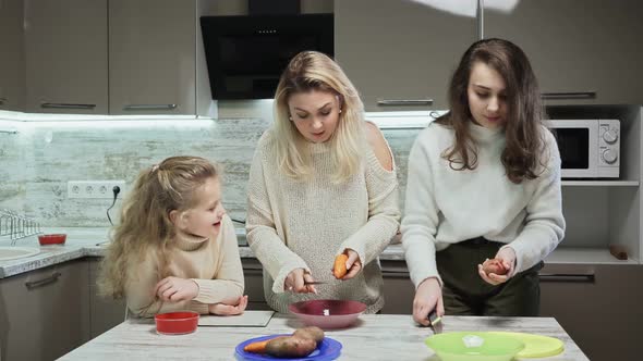 Young Mother and Two Her Daughters Cooks Salad at Kitchen