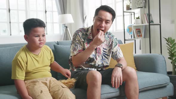 Happy Asian Father And His Son Are Watching Tv While Eating Potato Chips At Home