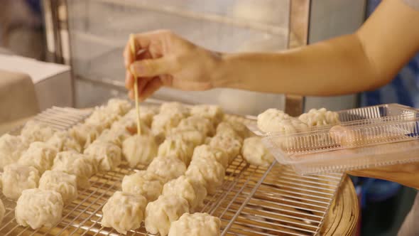 Vendor picking dumplings from bamboo steamer, preparing takeway order