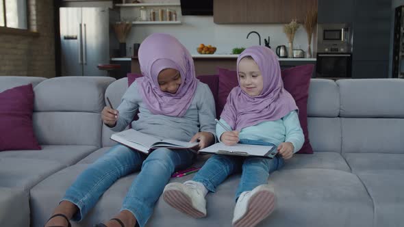 Lovely Preadolescent Muslim Sisters in Hijabs Drawing Picture with Colorful Pencils at Home