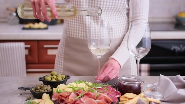 Woman Pouring Wine to a Glass From a Bottle at Domestic Kitchen with Meat and Cheese Plater on the