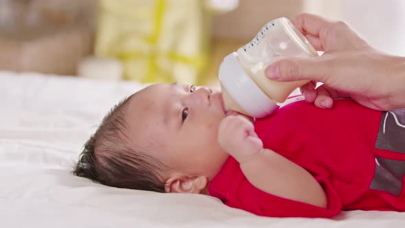 Close up hand of mother holding milk bottle Newborn baby lying on bed drinking milk