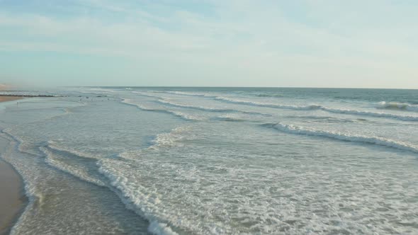 Few Surfers on Empty Beach with Perfect Waves in Sunset Light and White Foam Waves, Aerial Forward