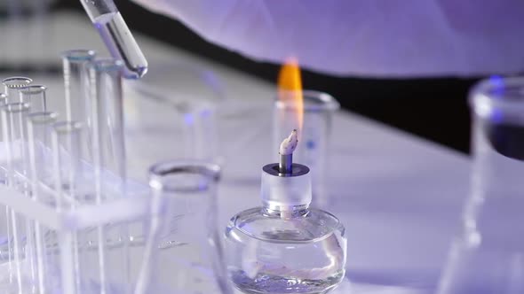 Close-up hand medical virologist holding test tube with biomaterial over fire