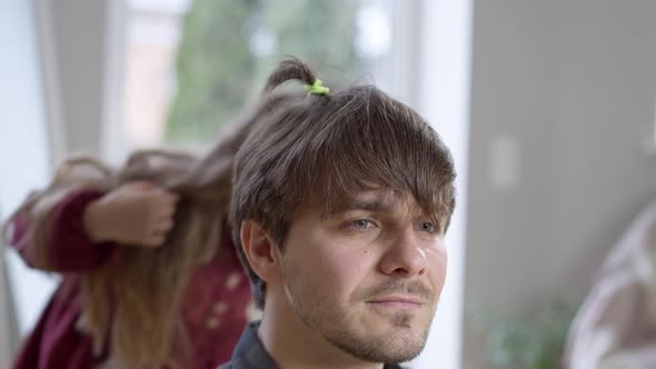 Closeup Face of Sad Young Brunette Man with Cheerful Blurred Little Girl Making Ponytails at