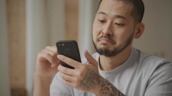 Young Adult Tattooed Asian Man is Surprised While Browsing on His Smart Phone