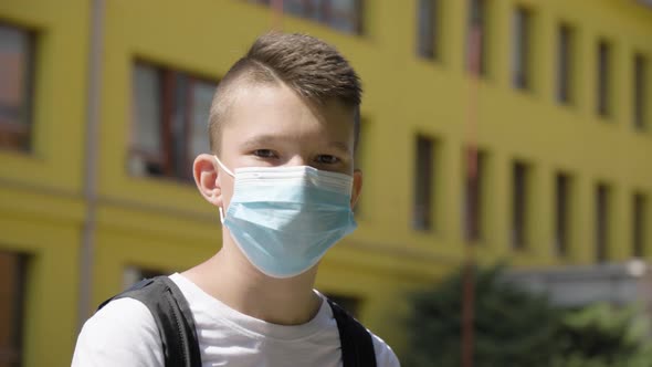 A Caucasian Teenage Boy Puts on a Face Mask and Looks at the Camera  Closeup  a School