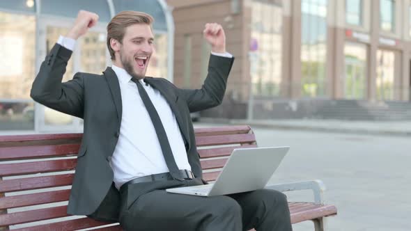 Businessman Celebrating Success on Laptop While Sitting Outdoor on Bench