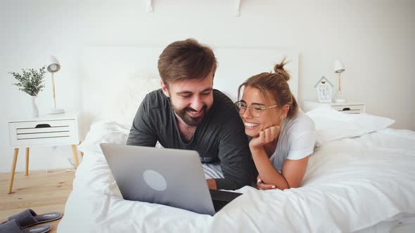 Young Couple in Pajamas Lying on Bed and Using Laptop in Cozy Bright Bedroom Slow Motion