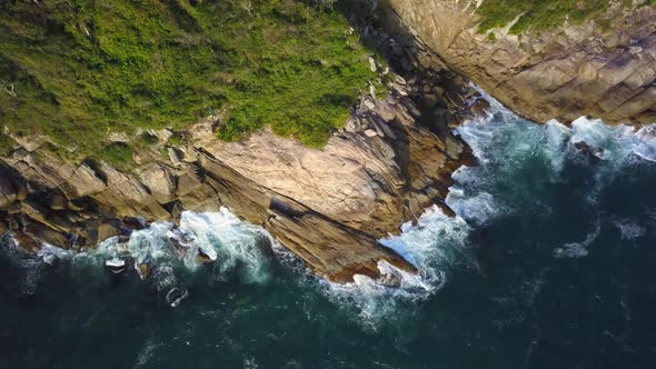 Aerial top down view of sea waves hitting on the low cliffs near Bombinhas. Wide shot