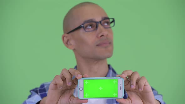 Face of Happy Bald Hipster Man Thinking While Showing Phone