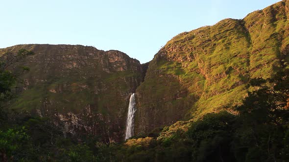 A picturesque waterfall tumbling down plant-covered cliffs into the river and valley below