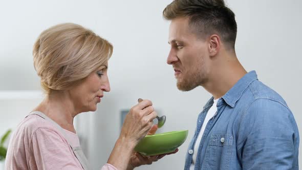 Overprotective Mother Feeding Her Adult Son With Spoon, Relations in Family