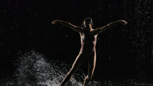 Wet Young Woman in a Tight Beige Swimsuit Is Dancing on the Floor Under the Rain and Splashes of