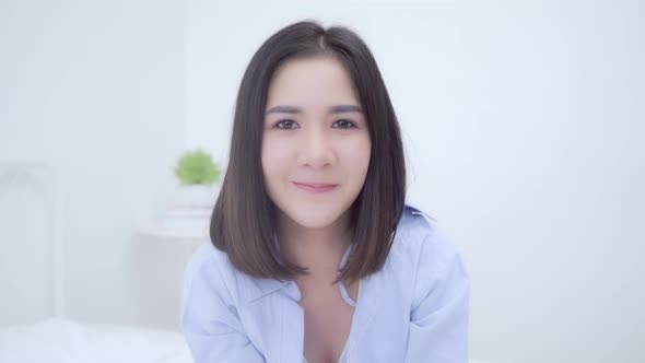 Asian Chinese woman feeling happy smiling   looking to camera while lying bed in bedroom.