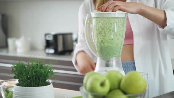 Female Prepares a Smoothies in the Kitchen Puts the Green Vegetables Ingredients and Mixes in a