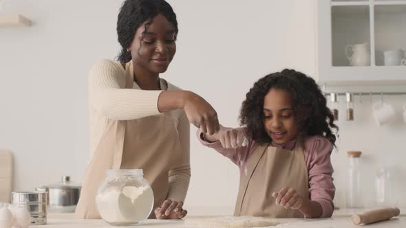 Cheerful African American Mother and Daughter Pouring Flour on Dough Preparing Pastry at Kitchen