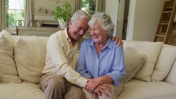Smiling caucasian senior couple hugging each other while sitting on the couch at home