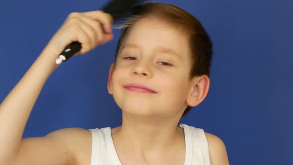Portrait of a cheerful caucasian boy 7 years old combing his hair with a massage brush.
