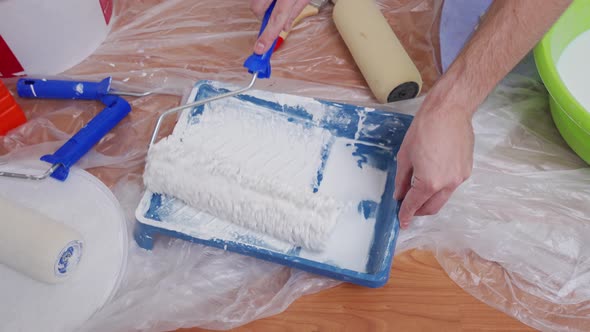 Closeup of Male Hands Drive a Paint Roller Over a Pallet with White Paint Picking Up Paint