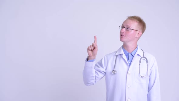 Happy Young Blonde Man Doctor Thinking While Pointing Up