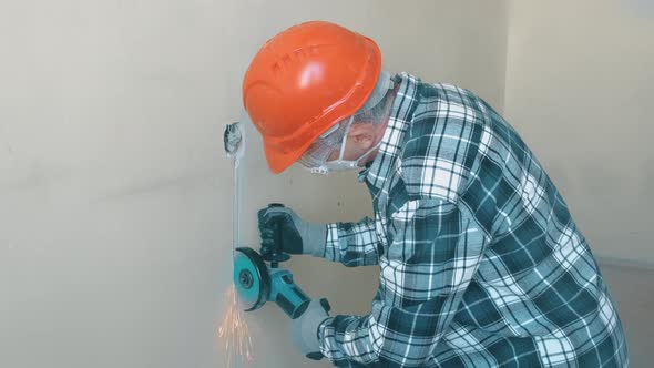 An Elderly Worker in an Orange Helmet and Protective Glasses with an Angle Grinder for Cutting Metal