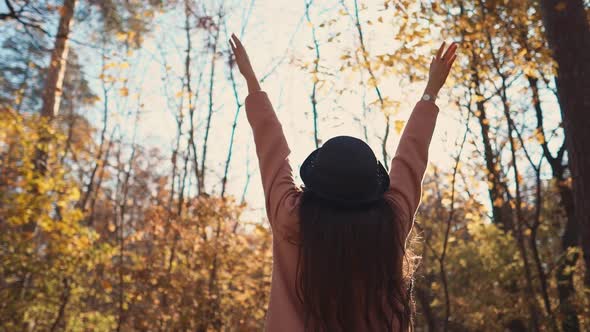 Young Brunette Girl Is Standing Alone in Autumn Forest and Lifting Hands, Back