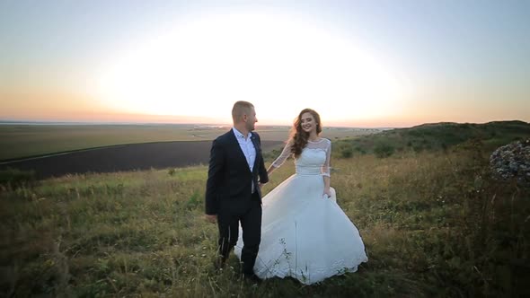 Bride and Groom Walking on the Grass Field in Love with Her Wedding Day