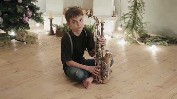 Young Musician, Saxophonist Sitting on the Floor in the Room of the House on the Background of