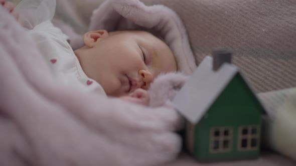 Closeup Portrait Cute Newborn Caucasian Girl Lying on Bed with Blurred Toy House