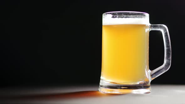 Refreshment Golden Beer in Big Mug with White Fluffy Foam Rotation Isolated at Black Background