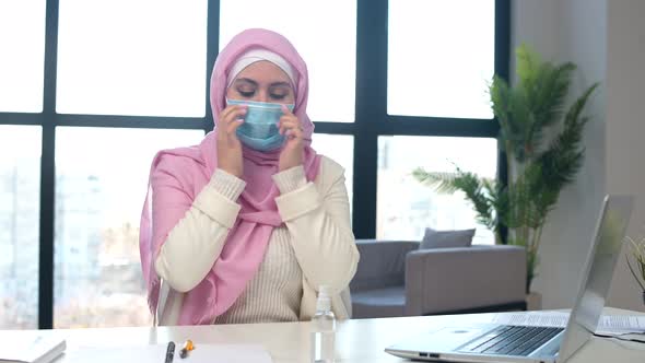 Muslim Woman Wearing Hijab Puts Medical Mask on the Face Sitting at Office
